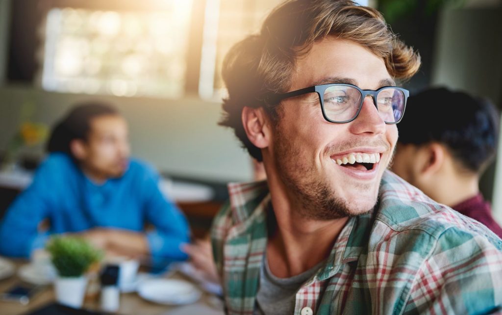 Sharing laughs over coffee Shot of a smiling young man sitting at a cafe table with friends in the background